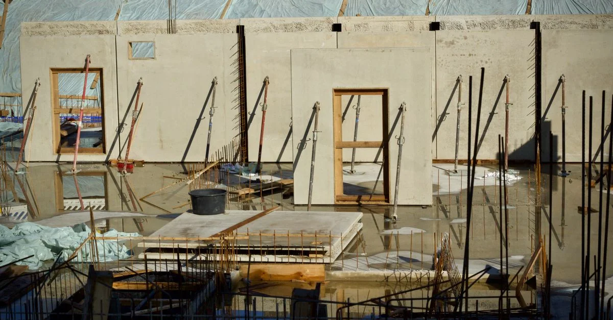 Obra en construcción con muros de hormigón y marcos de ventanas y puertas iluminados con luz natural.