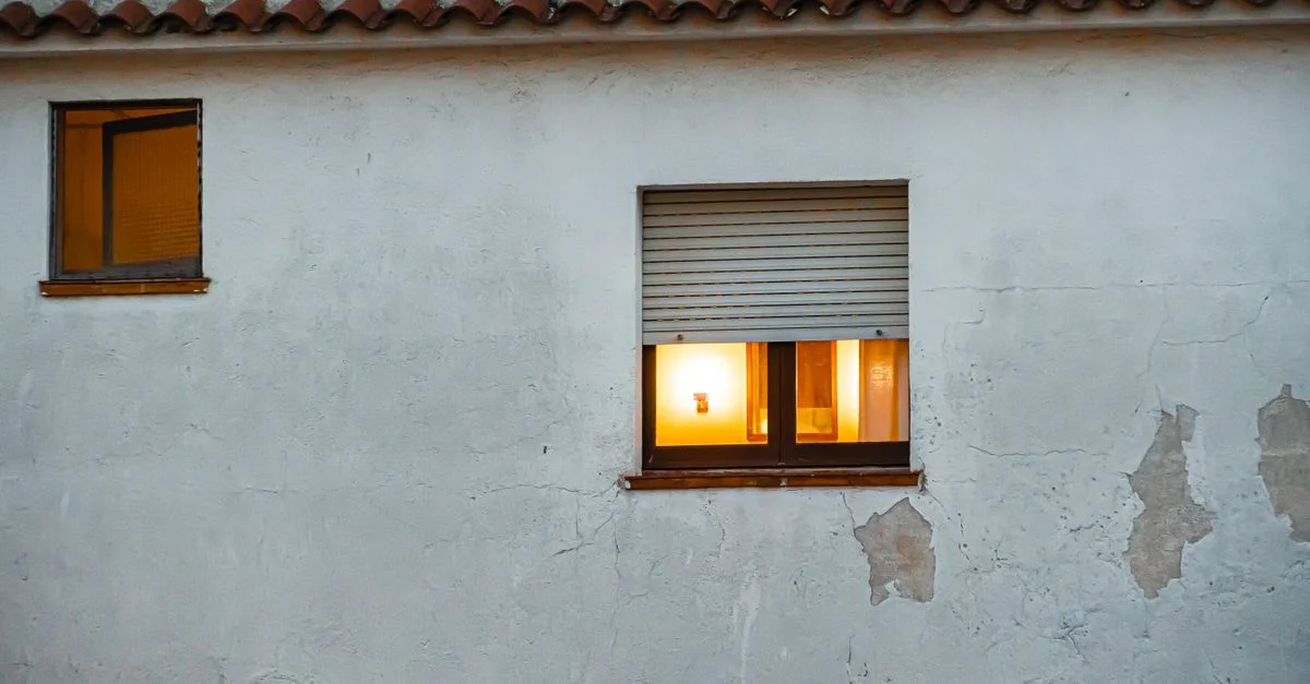 Vista exterior de una casa con ventanas iluminadas y pared de yeso texturizada, creando un ambiente cálido.