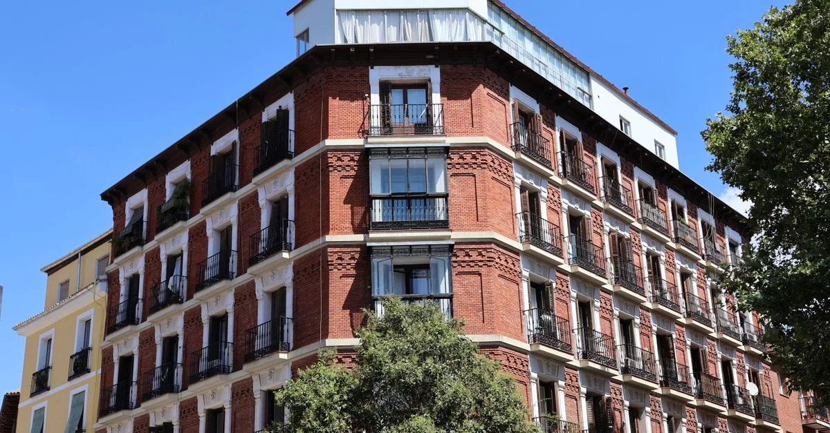 Un clásico edificio de apartamentos de ladrillo rojo en Madrid con un cielo azul claro como telón de fondo.