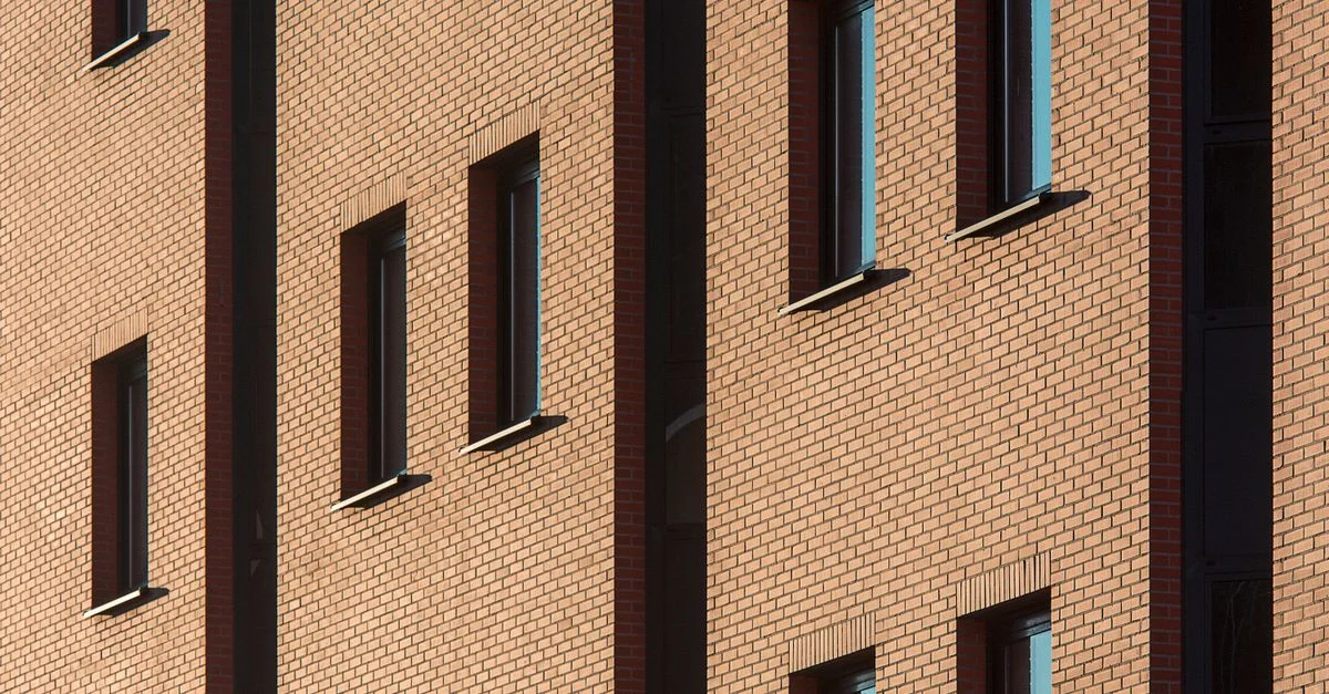 Primer plano de la fachada de un edificio de ladrillo con la luz solar resaltando las ventanas, un diseño arquitectónico urbano clásico.