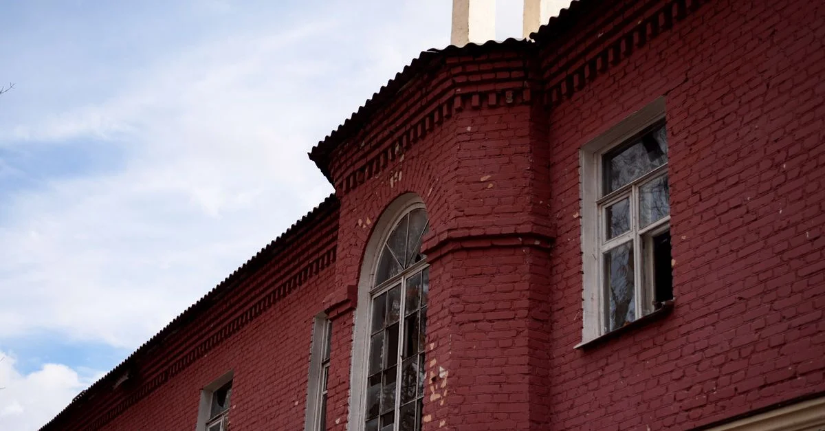 Una vista detallada de la fachada de un edificio de ladrillos rojos con una ventana en arco bajo un cielo azul.