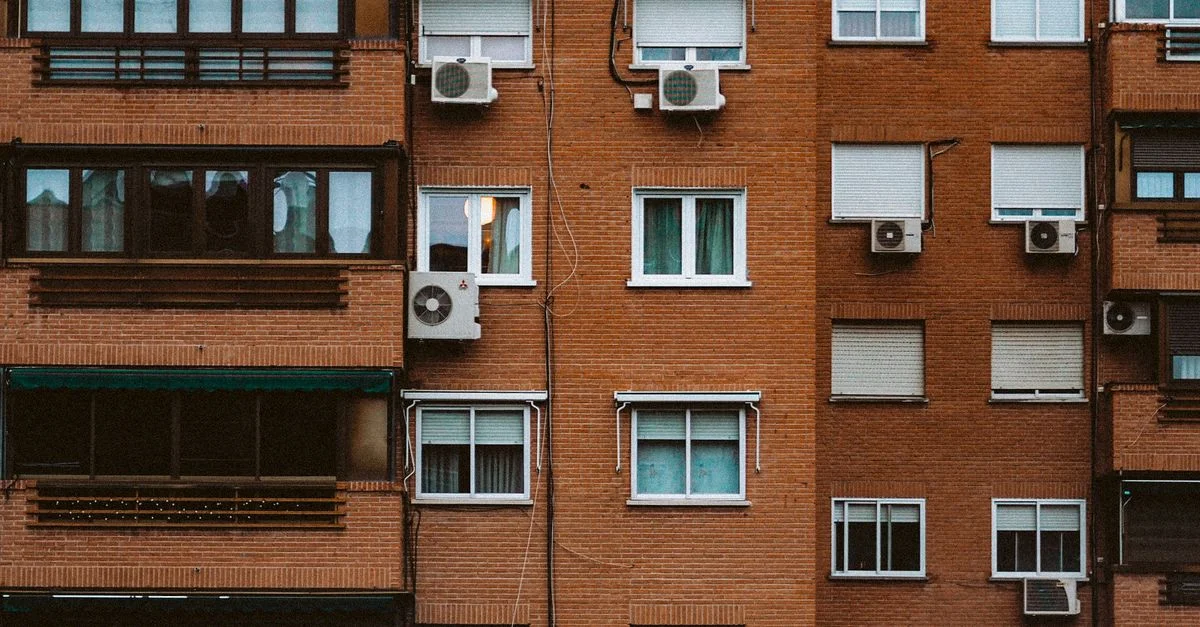 Una vista detallada de la fachada de un apartamento de ladrillos naranjas con ventanas y aires acondicionados.
